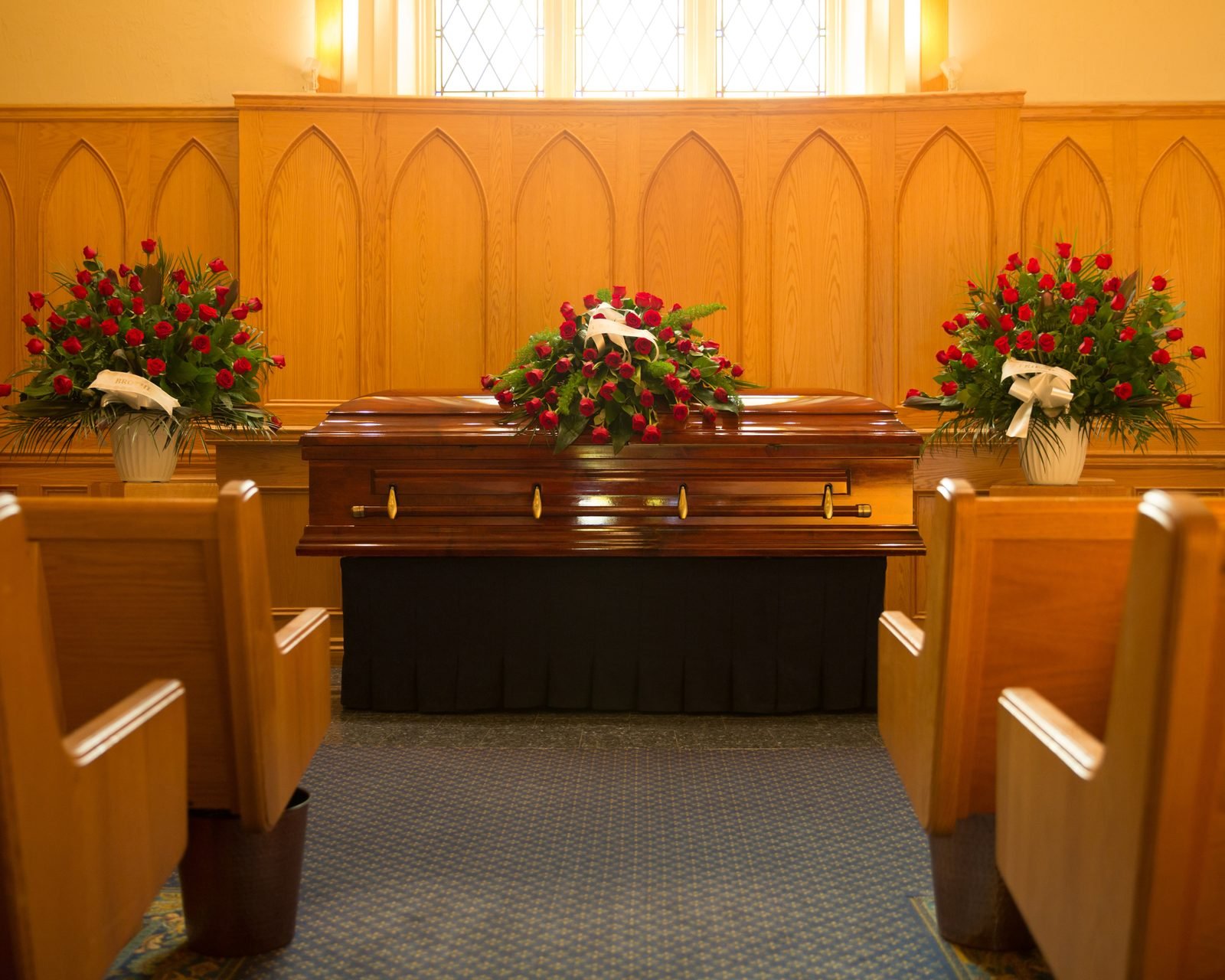 A chapel setting with a casket and red floral arrangements.