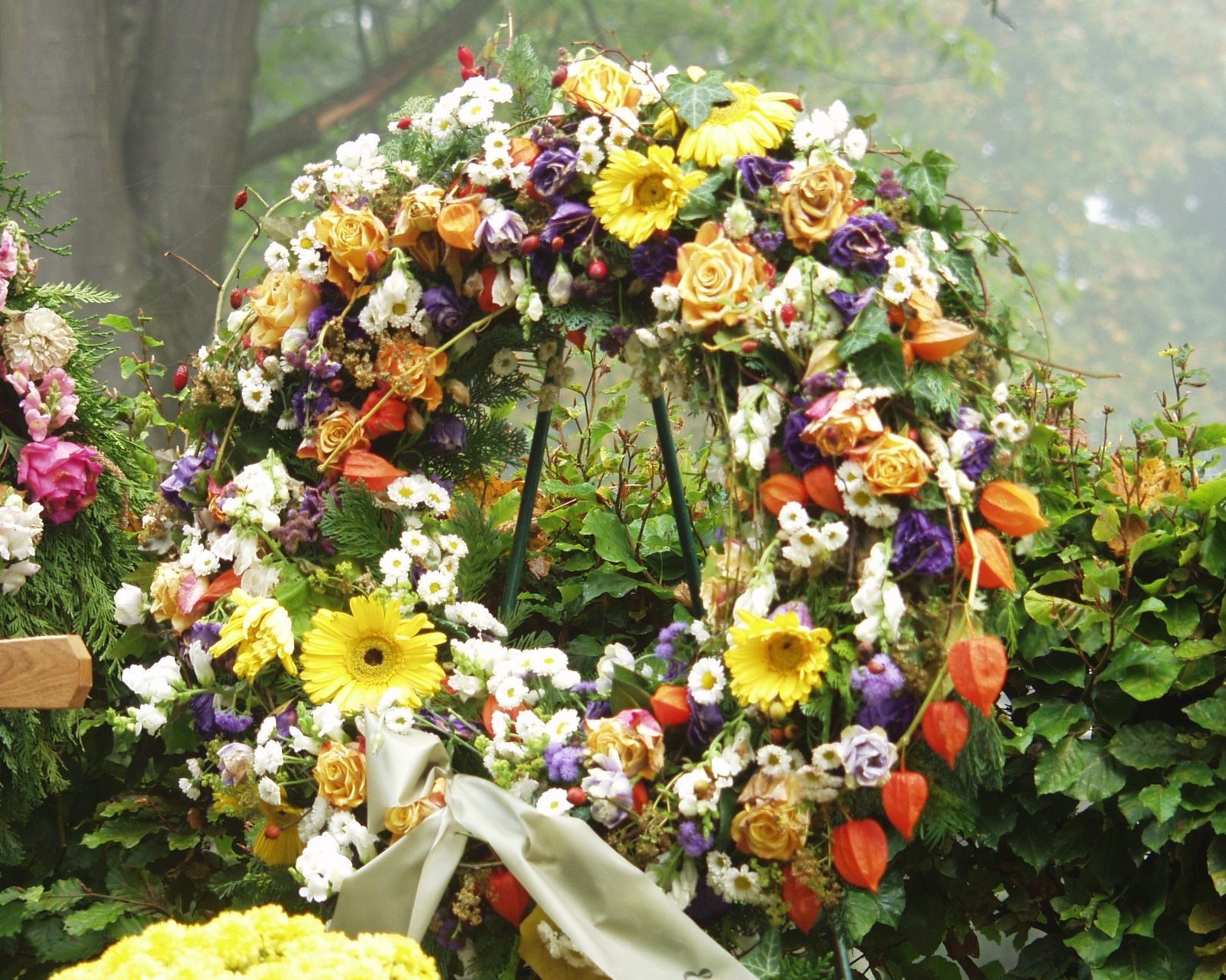 A colorful standing floral wreath of roses, daisies, and greenery.