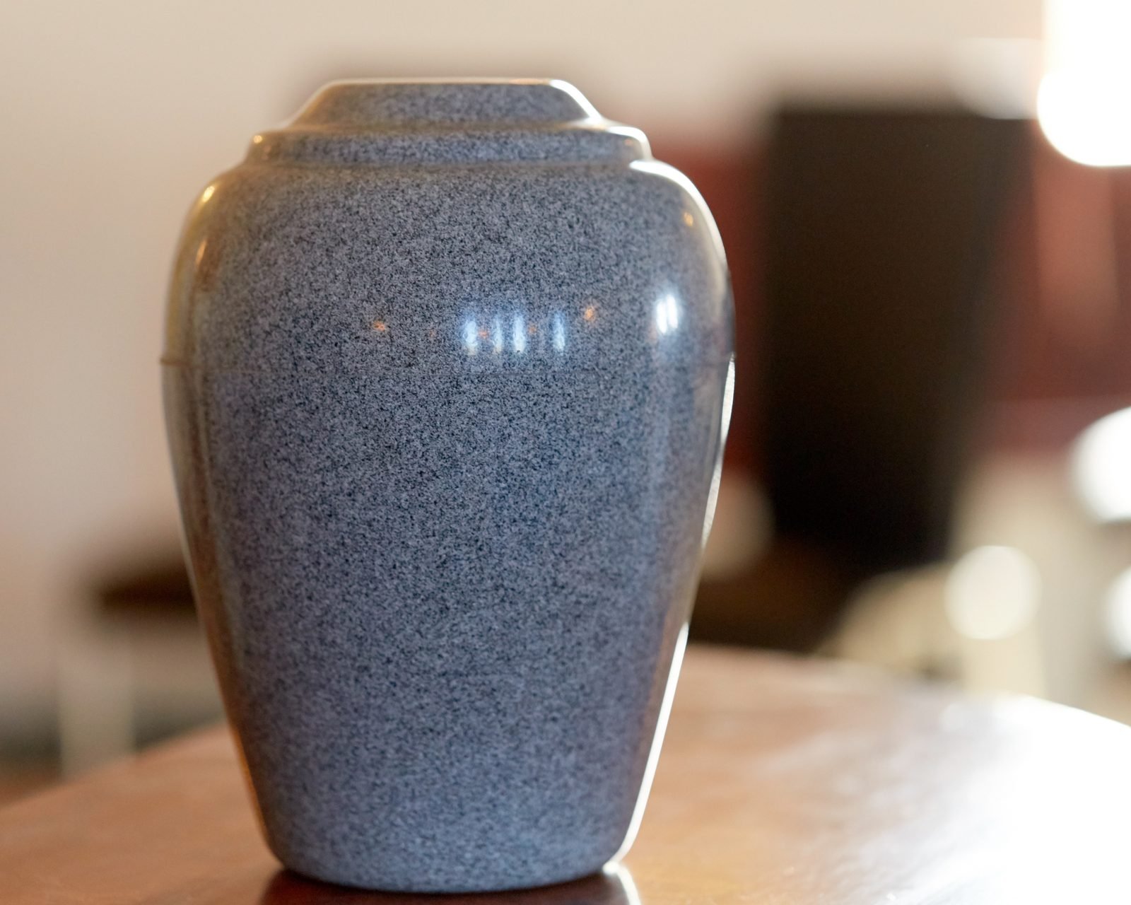 A blue-gray cremation urn on a wooden table.