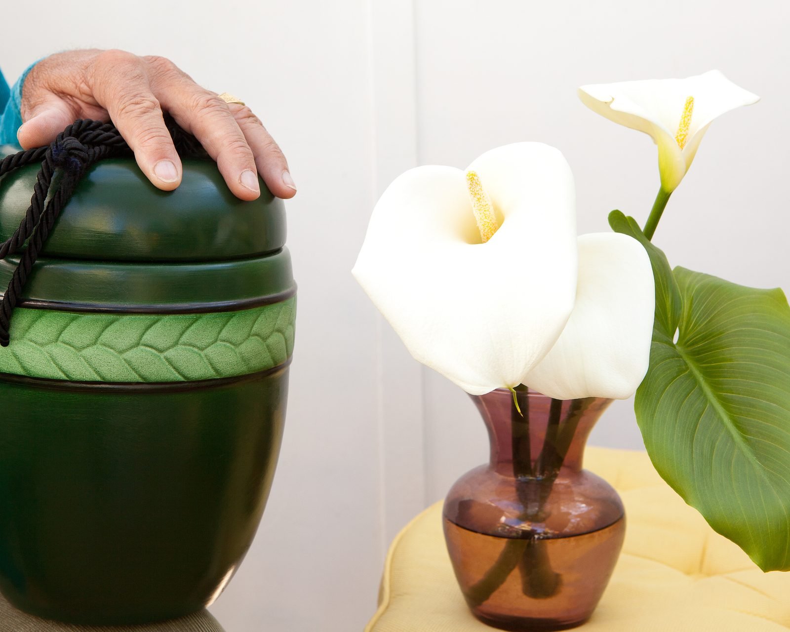 A green cremation urn beside white calla lilies.